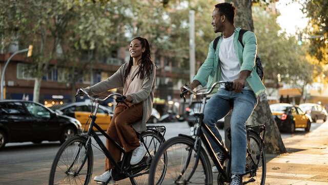 "Couple à vélo explorant une rue ensoleillée de Barcelone, une excellente idée de coffret cadeau citytrip. "