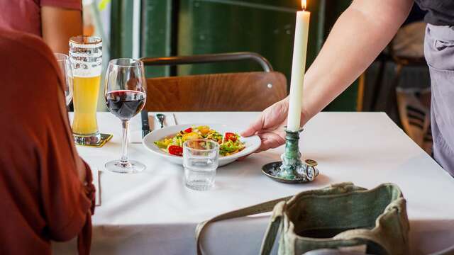 Ober die een salade presenteert aan een tafel voor twee, een sleutelmoment van een gourmetdiner.