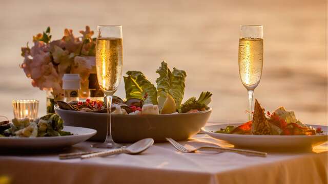 Mesa preparada para una cena romántica con ensalada y copas de champán.