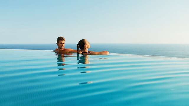 Pareja de recién casados abrazándose en una piscina infinita con vistas al mar durante su luna de miel.