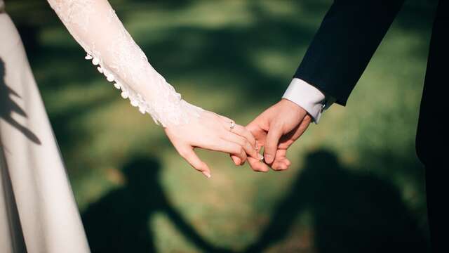 Primer plano de las manos de una pareja de novios, vestidos de boda, entrelazadas.
