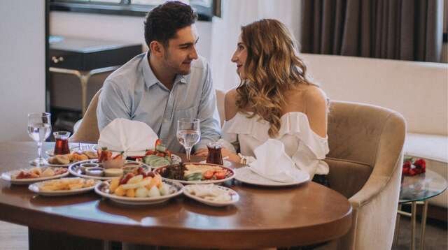 Pareja joven disfrutando de un aperitivo en el salón privado de su espaciosa habitación de hotel.