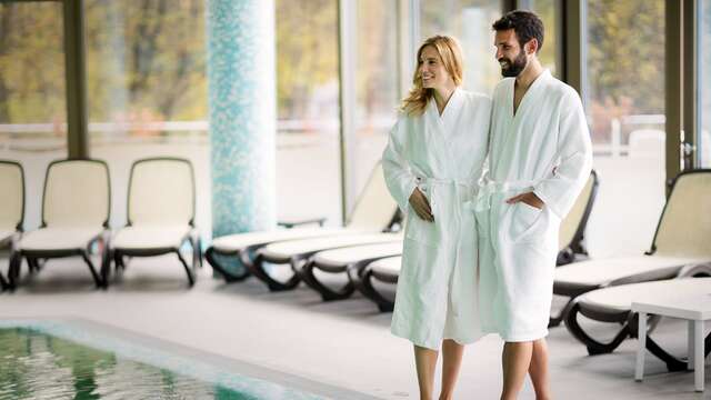 Pareja sonriente en albornoz, disfrutando de un momento de tranquilidad junto a la piscina de un lujoso spa.