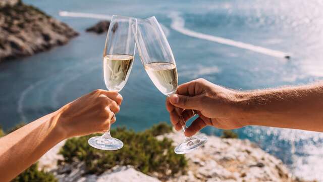 Dos copas de cava brindando frente al mar durante una puesta de sol romántica.