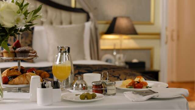 Desayuno completo y selecto servido en una bandeja a los pies de la cama de una suite de hotel.