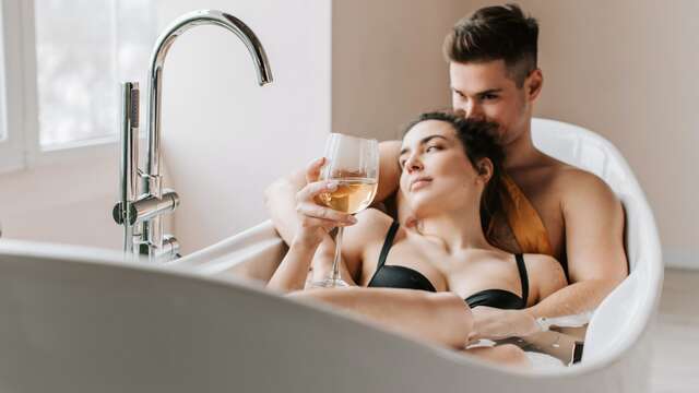 Pareja joven disfrutando de un momento romántico en un jacuzzi, mientras ella sostiene una copa de vino.
