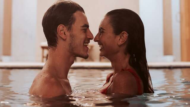 Pareja mirándose cómplice mientras se relajan juntos en la piscina de un hotel.