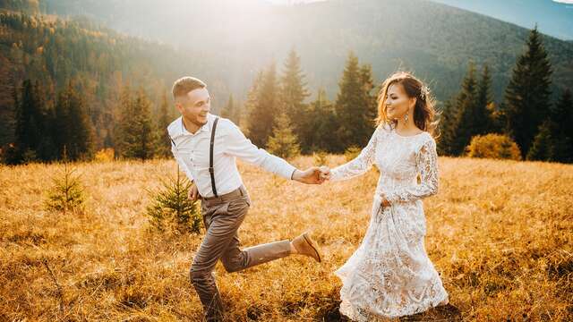 Pareja de recién casados paseando por un prado verde con un impresionante paisaje de montaña de fondo.