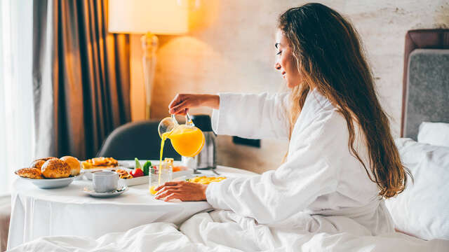 Mujer en albornoz sirviéndose zumo de un desayuno de lujo servido en la propia habitación del hotel.