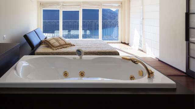 Lussuosa camera d'hotel con letto matrimoniale, jacuzzi privata e balcone con vista sul mare.