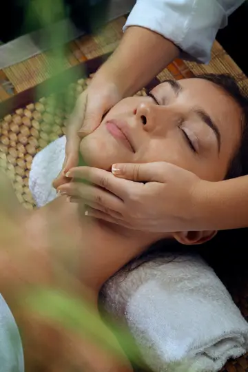 A woman receives a relaxing facial massage from a therapist's hands at a tranquil spa.