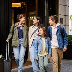 Happy family, two adults and two children, exiting a hotel with a suitcase.