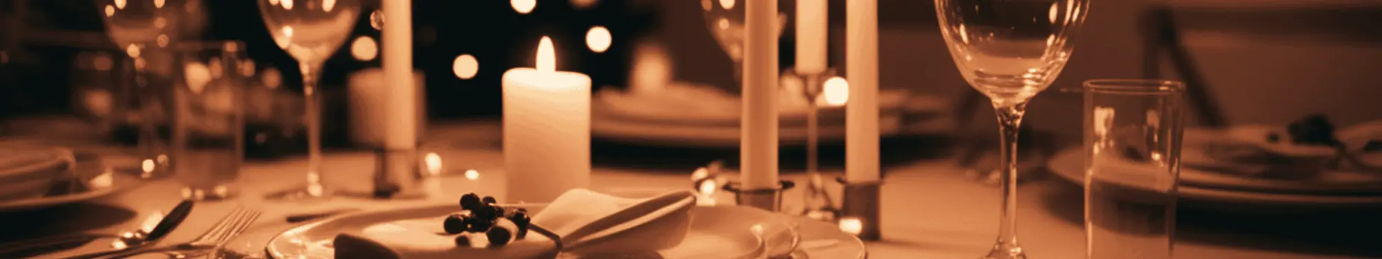 A warmly lit table setting with a burning candle, wine glasses, and dinnerware.