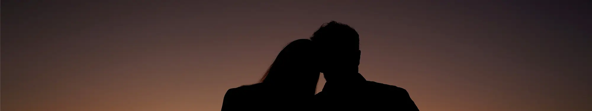 Silhouettes of two people leaning into each other against a warm sunset sky.