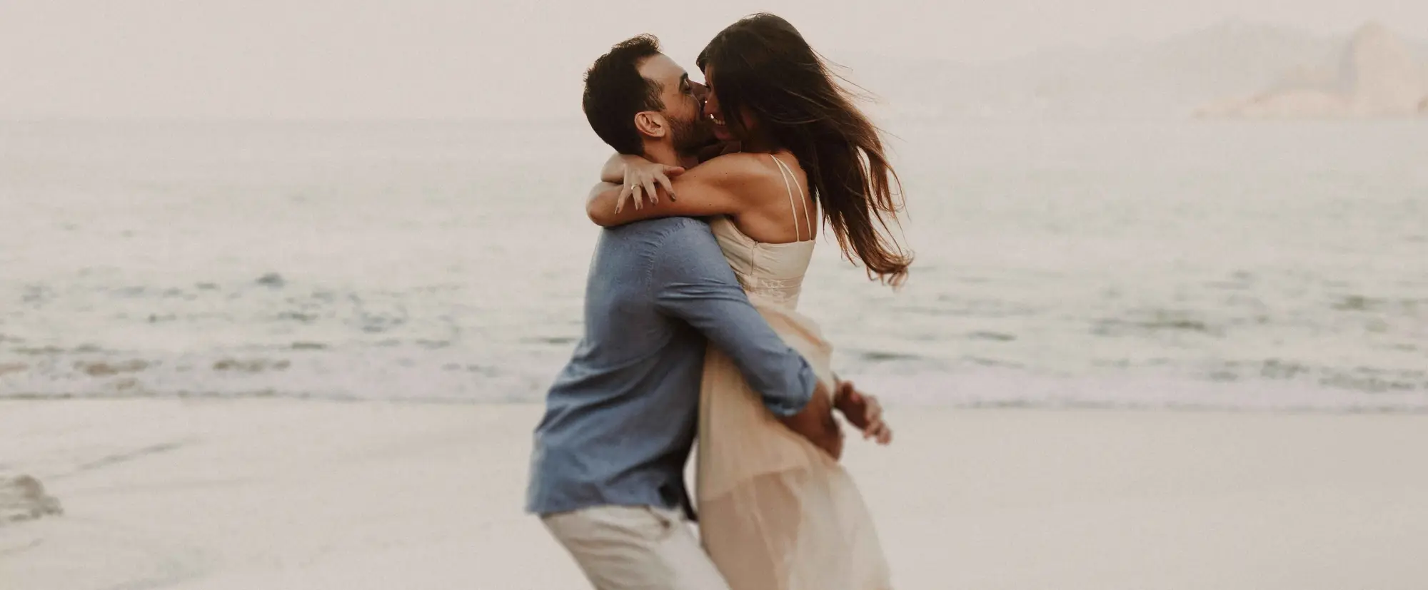 A loving couple shares a passionate kiss and hug on a sandy beach.
